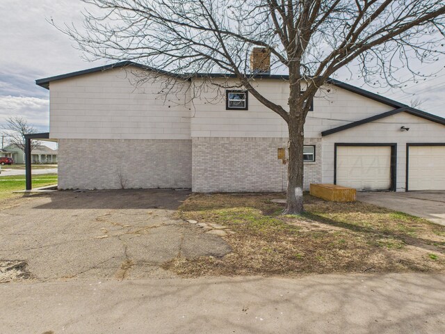view of side of property featuring driveway, an attached garage, a chimney, and brick siding