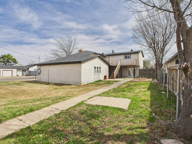 rear view of house featuring a lawn, stairs, and fence