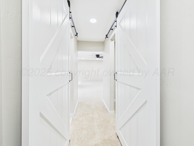 corridor featuring light carpet and a barn door