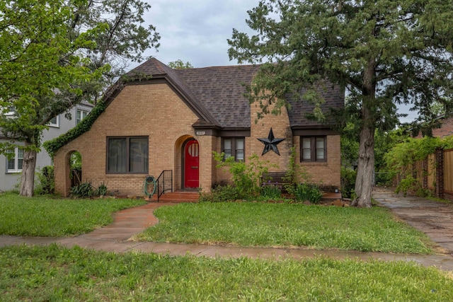 tudor-style house featuring brick siding, a shingled roof, and a front lawn