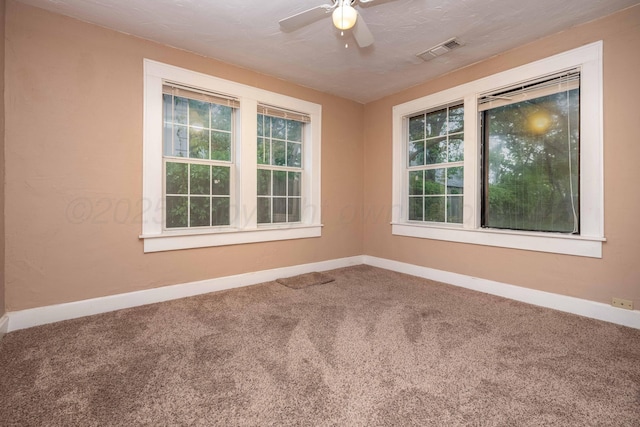 carpeted spare room featuring plenty of natural light, a ceiling fan, baseboards, and visible vents