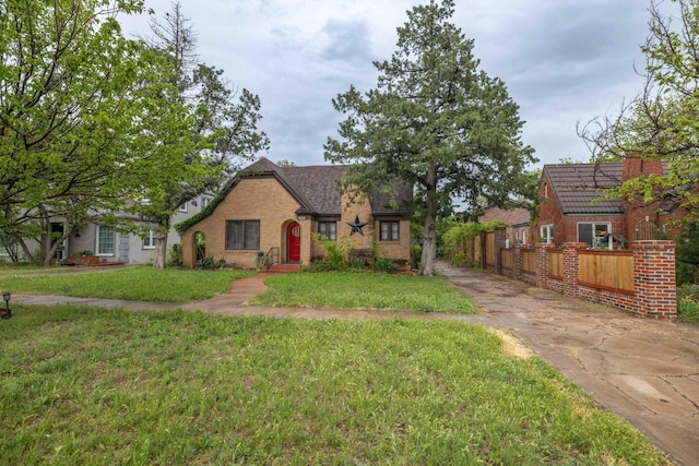 tudor house featuring brick siding, a front lawn, fence, and concrete driveway