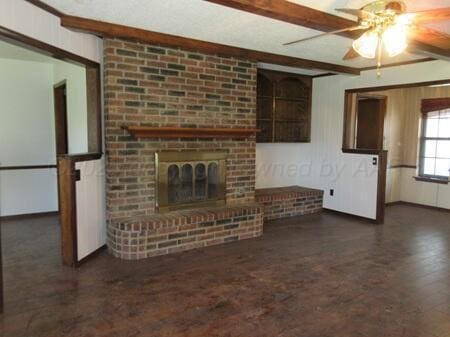 unfurnished living room with wood finished floors, a brick fireplace, beamed ceiling, and ceiling fan