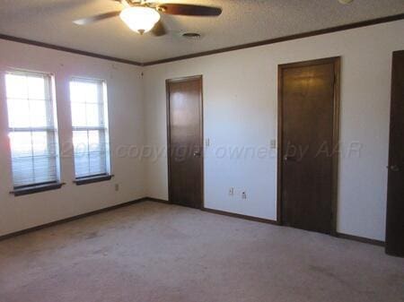 unfurnished bedroom featuring crown molding, ceiling fan, baseboards, and light carpet