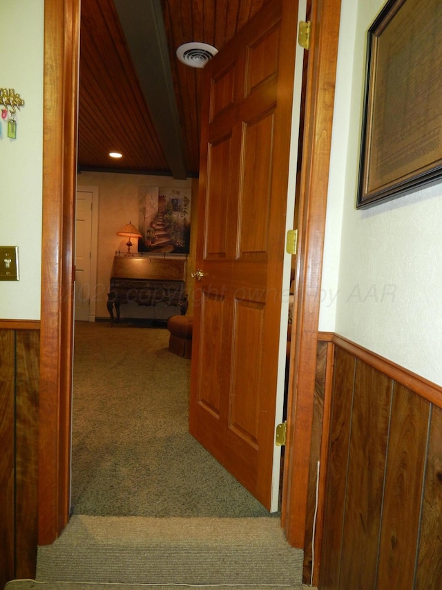 corridor featuring wooden walls, visible vents, a wainscoted wall, and carpet flooring