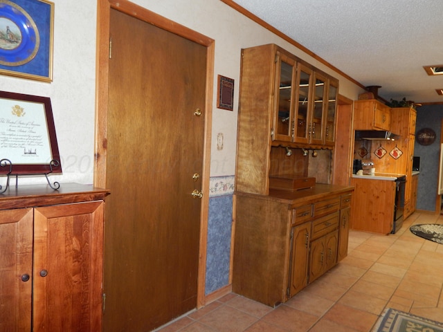 kitchen featuring under cabinet range hood, brown cabinetry, range, and a textured ceiling