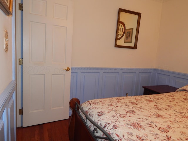 bedroom with a decorative wall, dark wood-style floors, and wainscoting