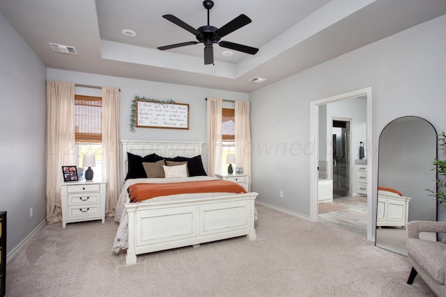 carpeted bedroom featuring a raised ceiling, ceiling fan, and connected bathroom