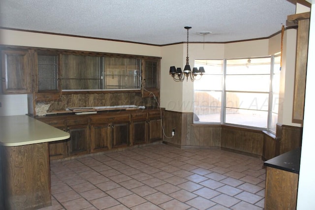 kitchen featuring a textured ceiling, a chandelier, wood walls, wainscoting, and crown molding