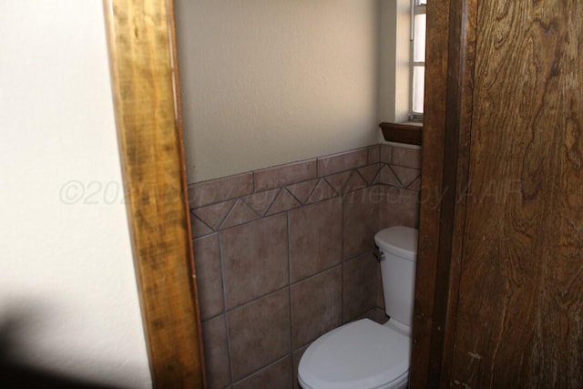 bathroom featuring a wainscoted wall, tile walls, and toilet