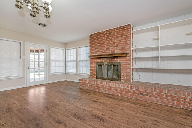 unfurnished living room with a fireplace, hardwood / wood-style floors, baseboards, visible vents, and an inviting chandelier
