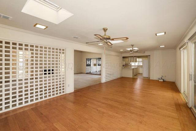 unfurnished living room with a skylight, ceiling fan, light hardwood / wood-style flooring, and ornamental molding