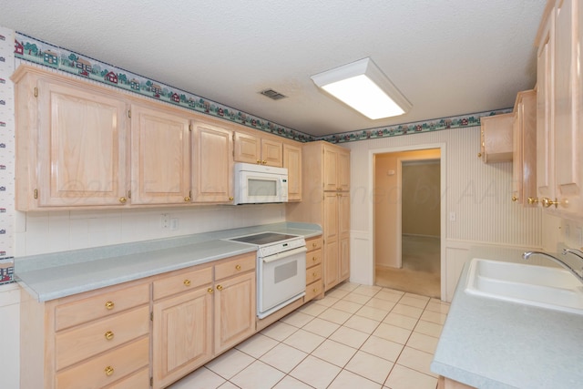 kitchen with white appliances, light brown cabinets, a sink, wallpapered walls, and light countertops
