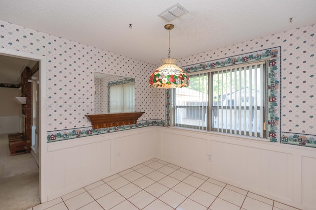 unfurnished dining area featuring wallpapered walls, a wainscoted wall, a textured ceiling, a decorative wall, and light tile patterned floors