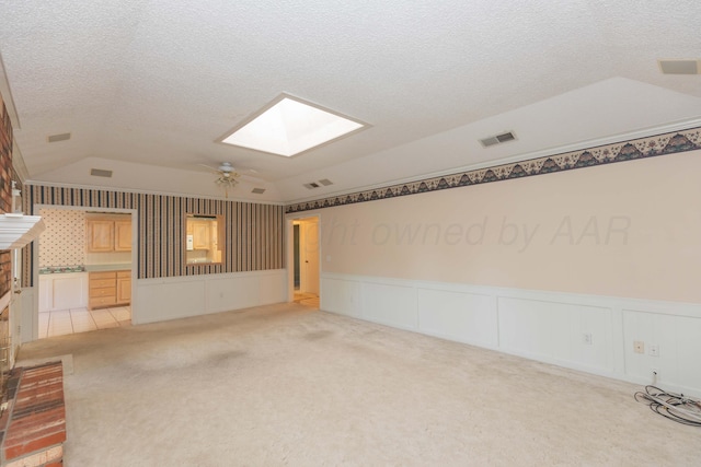unfurnished living room with a skylight, lofted ceiling, light carpet, wainscoting, and ceiling fan
