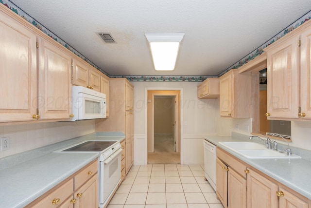 kitchen featuring white appliances, light brown cabinetry, a sink, and a textured ceiling