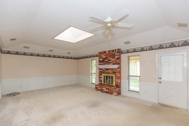 unfurnished living room featuring vaulted ceiling, wainscoting, a skylight, a ceiling fan, and a brick fireplace
