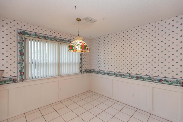 unfurnished room featuring wallpapered walls, a wainscoted wall, light tile patterned floors, a decorative wall, and a textured ceiling