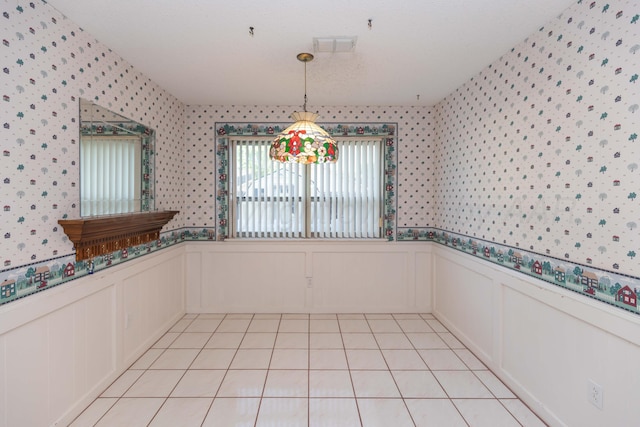 unfurnished dining area with wallpapered walls, a wainscoted wall, light tile patterned flooring, a decorative wall, and a textured ceiling