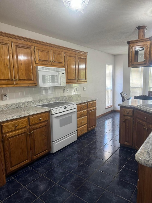 kitchen with tasteful backsplash, light stone countertops, dark tile patterned flooring, and white appliances