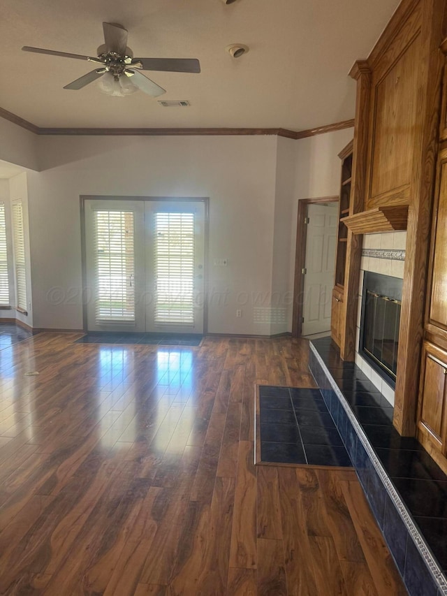 unfurnished living room featuring dark hardwood / wood-style flooring, ceiling fan, crown molding, and a tiled fireplace