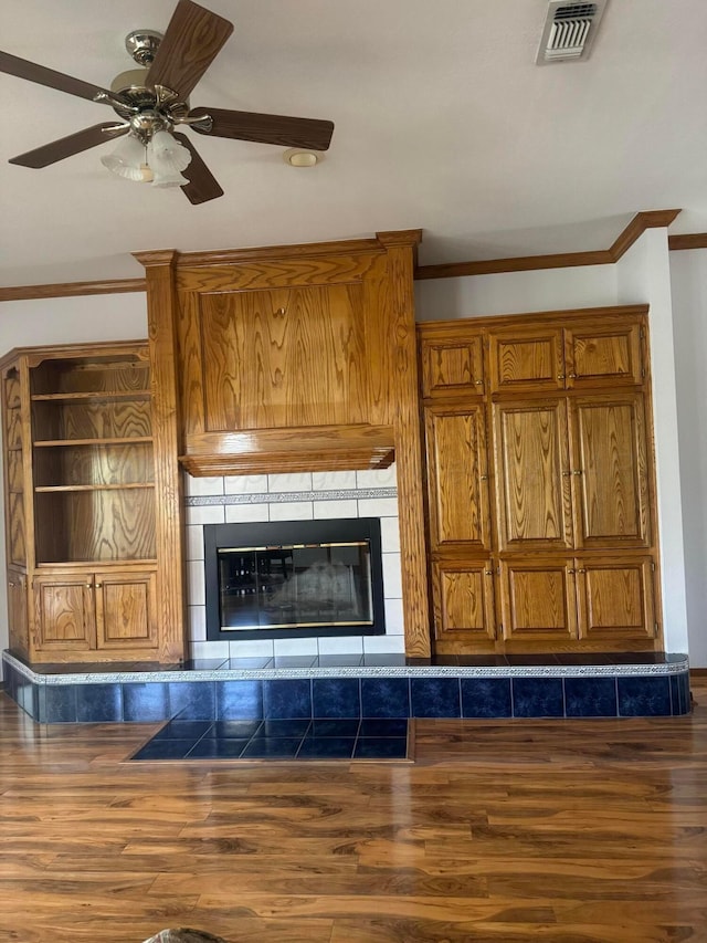 unfurnished living room featuring a tiled fireplace, ceiling fan, dark wood-type flooring, and ornamental molding