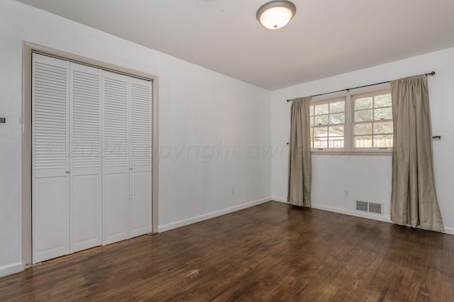 unfurnished bedroom featuring dark wood-style floors, baseboards, visible vents, and a closet