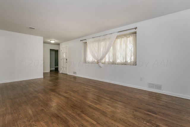 spare room featuring dark wood-style flooring, visible vents, and baseboards