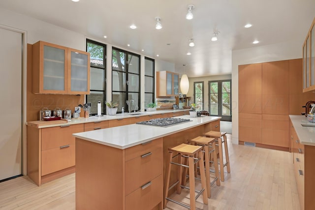 kitchen with a kitchen bar, stainless steel gas cooktop, sink, a kitchen island, and light wood-type flooring