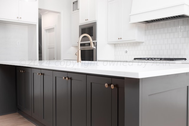 kitchen featuring decorative backsplash, light stone countertops, premium range hood, stainless steel appliances, and white cabinetry