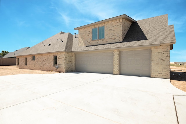 exterior space with brick siding, a shingled roof, an attached garage, and driveway