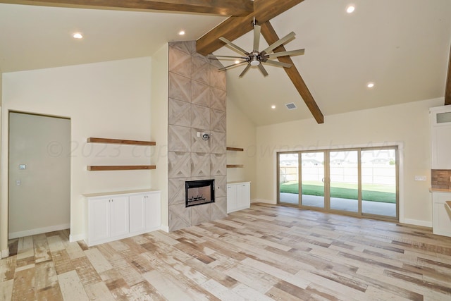 unfurnished living room with a fireplace, ceiling fan, high vaulted ceiling, beamed ceiling, and light hardwood / wood-style floors