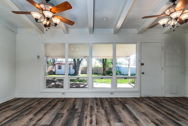 empty room with a ceiling fan, beam ceiling, a wealth of natural light, and dark wood-type flooring