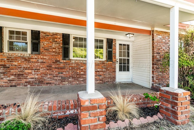 doorway to property with covered porch and brick siding