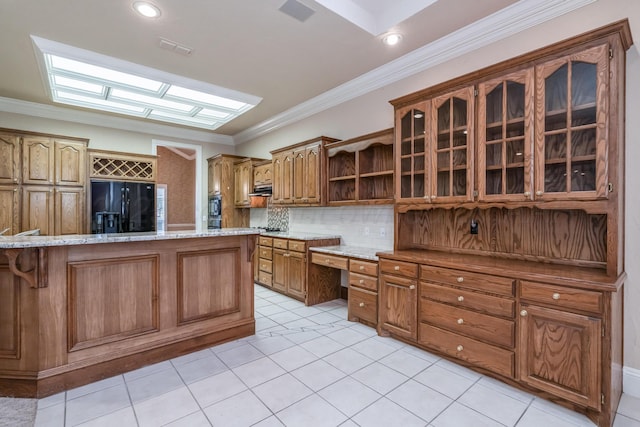 kitchen featuring glass insert cabinets, open shelves, brown cabinetry, black fridge, and crown molding
