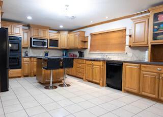 110 Dallam Ave, Dumas, TX 79029 - kitchen featuring black appliances, light tile patterned floors, open shelves, a kitchen bar, and a center island