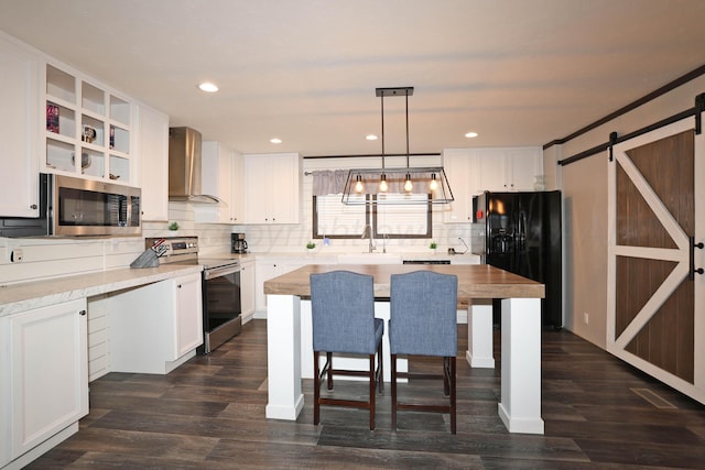 707 Trice St, Claude, TX 79019 - kitchen featuring wall chimney range hood, white cabinets, a barn door, stainless steel appliances, and a sink