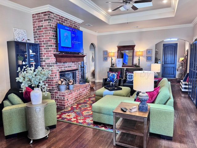 living room featuring dark hardwood / wood-style floors, a fireplace, ornamental molding, and a tray ceiling