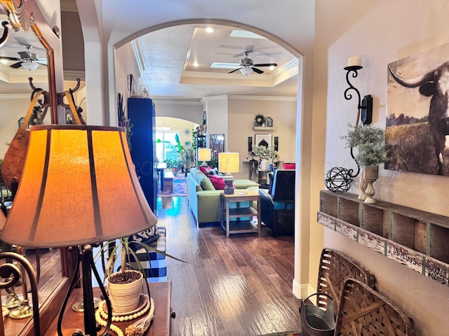 interior space with a raised ceiling, ornamental molding, ceiling fan, and dark hardwood / wood-style flooring