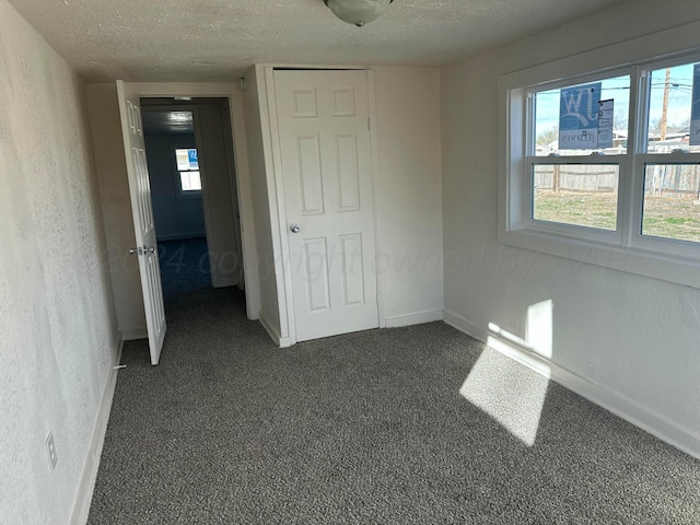 unfurnished bedroom featuring a textured ceiling, dark carpet, and a closet