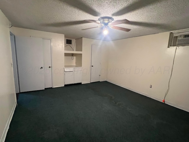 unfurnished bedroom featuring ceiling fan, dark carpet, a textured ceiling, and a wall unit AC