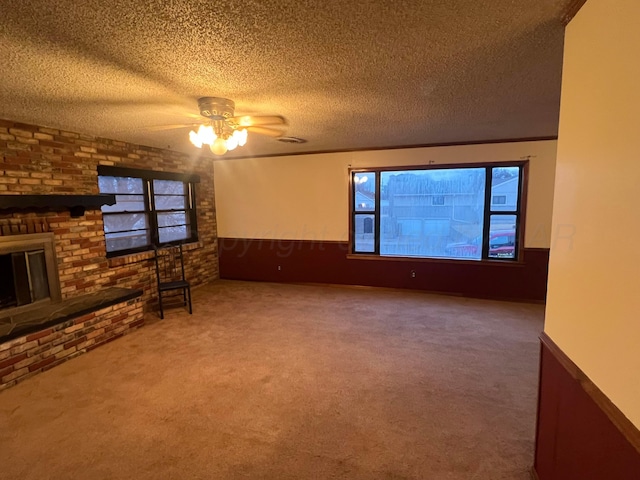 unfurnished living room featuring a brick fireplace, a textured ceiling, carpet flooring, ceiling fan, and brick wall