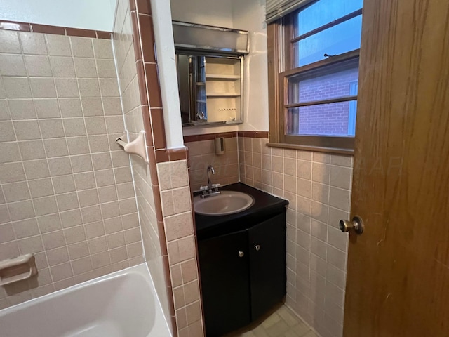 bathroom featuring tiled shower / bath combo, vanity, and tile walls