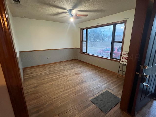 unfurnished room featuring dark hardwood / wood-style flooring, ceiling fan, and a textured ceiling