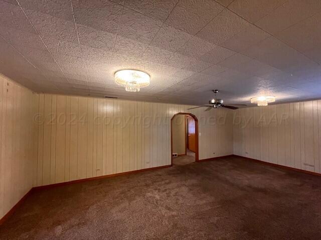 basement with ceiling fan, wooden walls, and dark carpet