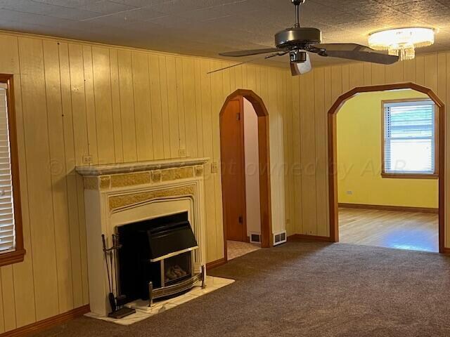 unfurnished living room featuring carpet, a fireplace, wood walls, and ceiling fan