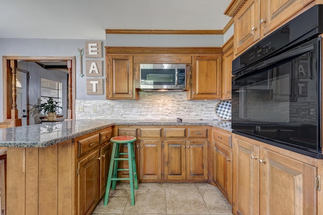 3409 Harmony St, Amarillo, TX 79109 - kitchen with stainless steel microwave, black oven, brown cabinets, backsplash, and dark stone countertops