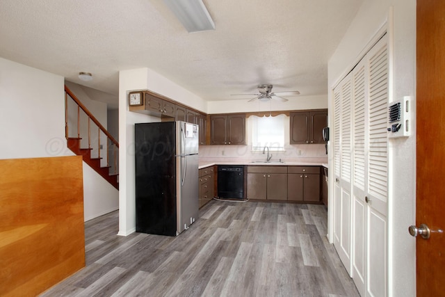 kitchen with wood-type flooring, black dishwasher, sink, stainless steel refrigerator, and dark brown cabinets