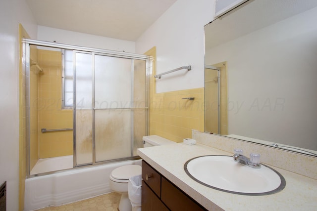 full bathroom featuring toilet, vanity, bath / shower combo with glass door, and tile walls