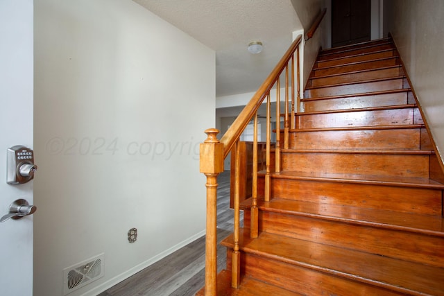 stairs featuring wood-type flooring and a textured ceiling